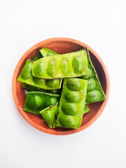 Raw Petai (Parkia Speciosa) or Bitter Bean in a wooden plate on a white background.