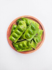 Raw Petai (Parkia Speciosa) or Bitter Bean in a wooden plate on a white background.