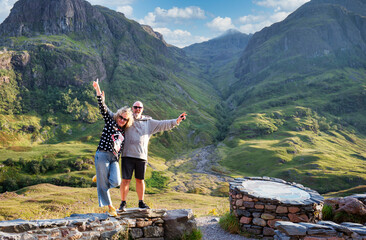 Happy mature couple raising arms in Glencoe Highlands landscape on holidays