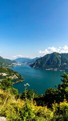 Panoramic vista of a tranquil lake nestled amidst verdant mountains under a clear, bright sky.