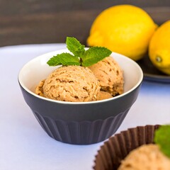 Creamy light brown ice cream scoops in a dark bowl, with fresh mint leaves on top