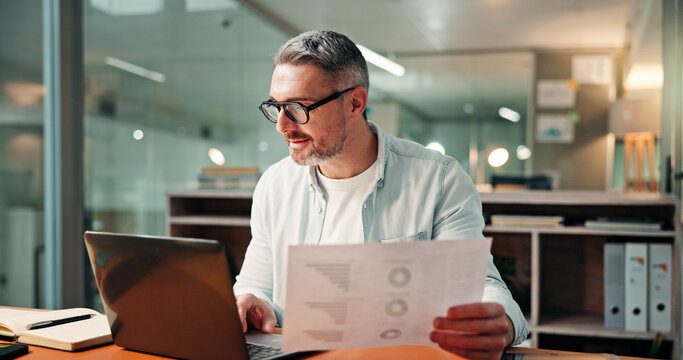 Mature, businessman and night with documents on laptop for performance review or analysis in office. Man, financial advisor or working late with paperwork, statistics or report deadline in workplace