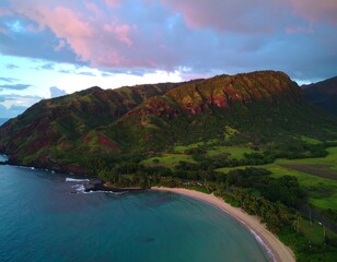 Lush green hills descend to a crescent beach, embraced by a tranquil turquoise ocean under a vibrant sunset sky