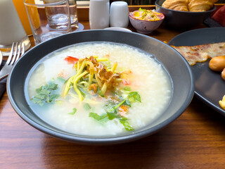 Savory Breakfast Dish: A vibrant bowl of congee is presented atop a wooden surface, surrounded by accompanying culinary delights.