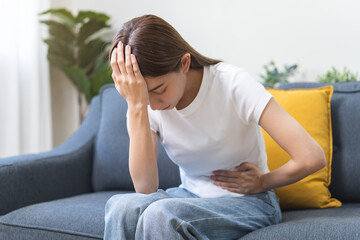 Sick asian young woman in pain, hand holding belly, stomach pain from food poisoning, girl hurt...