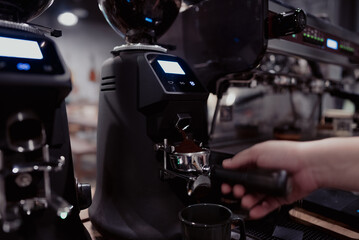 Close up of barista hand using coffee grinder machine in modern cafe, fresh ground coffee falling into portafilter, professional preparation of espresso drink with technology and precision.