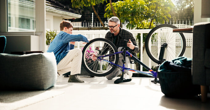 Father, child and bicycle maintenance for learning, helping and bonding with son at family home. Dad, kid and fix bike together for wheel repair, teaching and cycling hobby at patio with parent