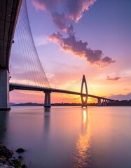 Fototapeta premium A magnificent cable-stayed bridge spans a tranquil waterway at sunset, showcasing a vibrant palette of warm colors reflected in the still water.