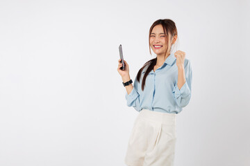Fototapeta premium Portrait happy young Asian woman holding a phone with fists clenched, excited by her success. She is a true winner, feeling the joy of victory with her mobile phone. isolated studio white background