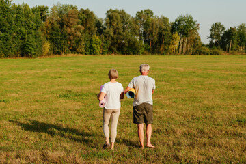 
Mature couple holding their yoga mats, walking away from the camera in a grassy field during sunset.
