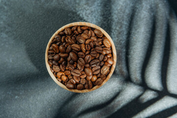 Coffee beans in wooden bowl with leaf shadow on dark background