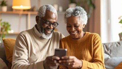 Joyful senior African American couple sitting on the sofa at home, happily using a smartphone together for entertainment or communication