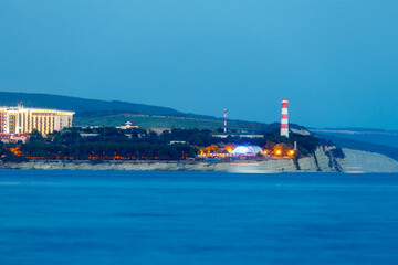 Geelndzhik lighthouse at sunset. Lighthouse stands on high rocky shore. ship sails. long exposure