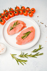 Two raw veal steaks with rosemary on white plate surrounded by cooking spices and vegetables