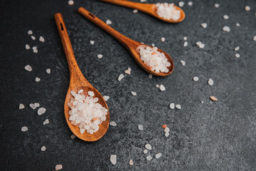 Wooden spoons with coarse pink himalayan salt on black stone surface