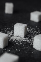 Cubes of sugar scattered on a dark surface with granulated sugar around