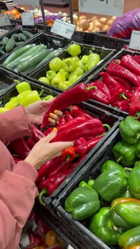 Hands selecting red and green peppers in a supermarket