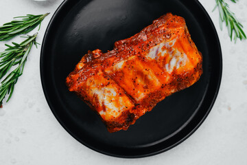 Spicy pork ribs on black plate with seasoning and herbs