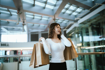 A cheerful young woman enjoys shopping in a luxury retail store, holding stylish bags with joy, glamour, and happiness in city life.