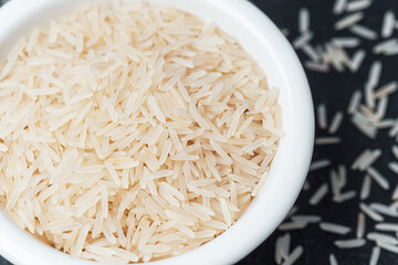 White rice in white ceramic bowl with scattered grains on dark surface