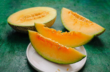 Cantaloupe melon slices arranged on a textured green surface with one half of the melon