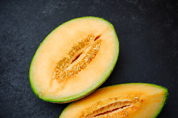 Juicy cantaloupe halves with seeds visible on a dark slate surface, top view.