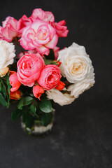 Fresh pink and white roses in a glass vase on a dark textured background, vibrant bloom close up