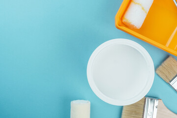 Open white paint bucket with brushes and roller on cyan background for painting supply and...