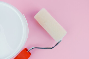 Top view of paint roller and open bucket on pink background for home painting preparation concept