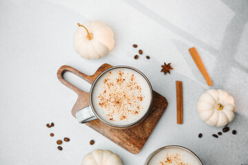 Warm frothy drink with cinnamon on wood board surrounded by mini pumpkins and coffee beans