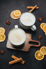 Warm spiced drinks with dried oranges and cinnamon sticks on dark surface