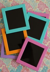 A collection of colorful photo frames stacked on a floral patterned surface creating a playful display