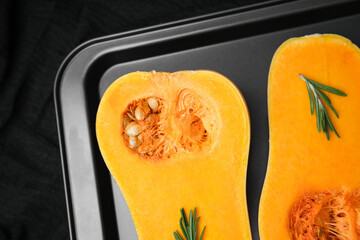 Halved butternut squash with rosemary on baking sheet, prepared for cooking.