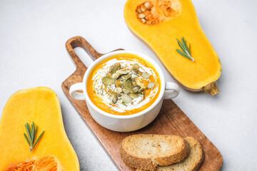 Butternut squash soup with seeds and cream served with bread on a wooden board and fresh squash