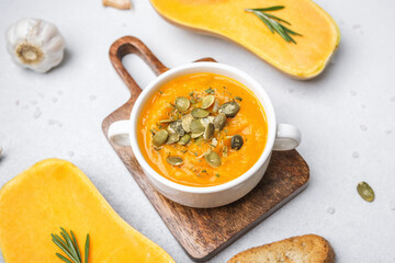 Bowl of creamy pumpkin soup garnished with pumpkin seeds, served with toasted bread and fresh...