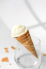 Closeup of waffle cone with creamy vanilla ice cream resting in clear glass on bright background with crumbs
