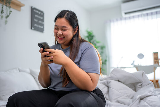 Asian young plus-size woman using smartphone in cozy room at home.