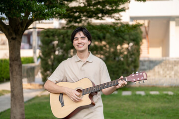 Portrait of Asian man musician playing an acoustic guitar in the garden. 