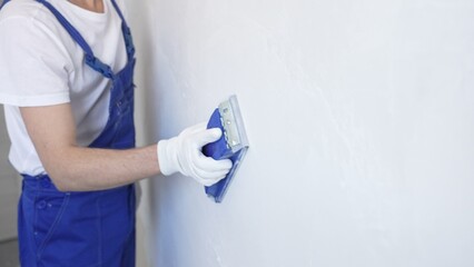 Unknown male construction worker wearing protective white gloves and blue construction coveralls,...