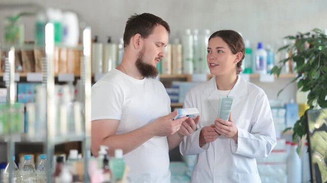 Man chooses ointment in modern pharmacy. Female pharmacist helps with choosing a medicine. High quality 4k footage
