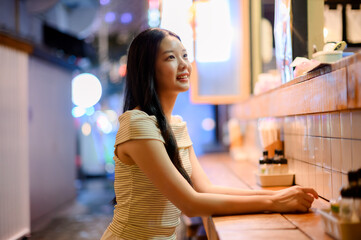 asian woman sitting at the bar counter in a japanese ramen restaurant, holding chopsticks with a...