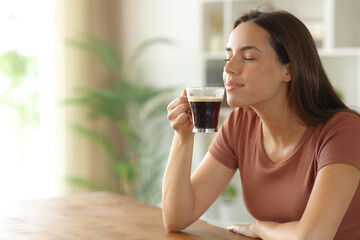 Woman relaxing smelling coffee aroma in a house interior