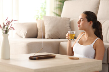 Relaxed woman smelling incense and drinking tea at home