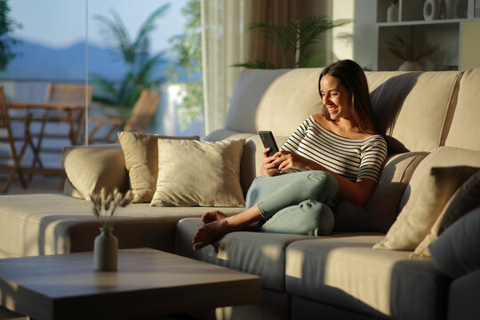 Happy woman using mobile phone sitting on a sofa in a house