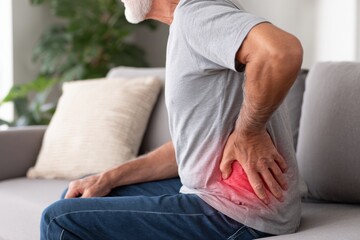 Elderly man on sofa clutching his lower back with a red glow, indicating discomfort and pain.