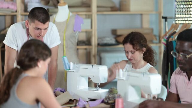 Focused young guy sewing while others working with sewing-machine and making details in dressmaking courses. High quality 4k footage