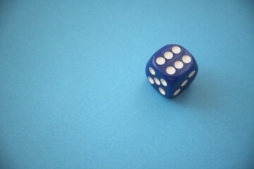 A blue die showing six dots placed on a blue background with copy space, representing luck or gaming.