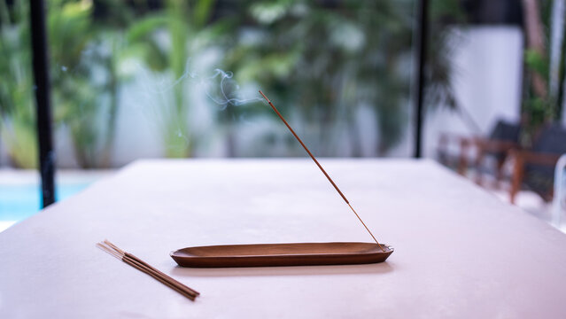 Burning incense stick with smoke in wooden holder, with extra incense sticks on the table, symbolizing meditation, relaxation, spirituality, and calming atmosphere.