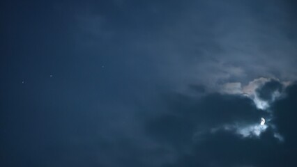 The moon shines through the clouds in the night sky with some stars