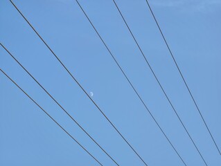 A view of power lines against a clear blue sky with a small moon